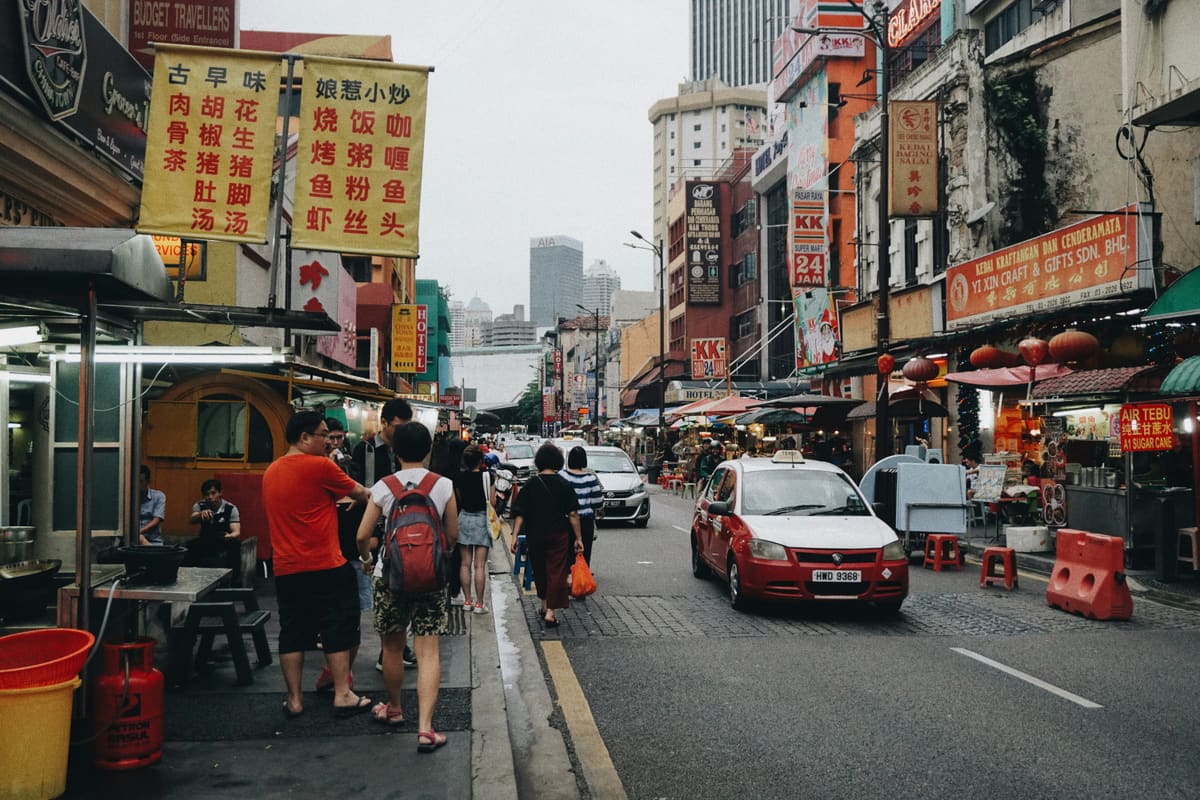 A busy street in Kuala Lumpur's Chinatown, with shophouses, food stalls and a taxi